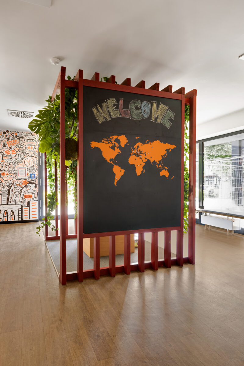 Interior of Staytoo Apartments with a welcome board featuring a world map, surrounded by plants and creative wall illustrations.