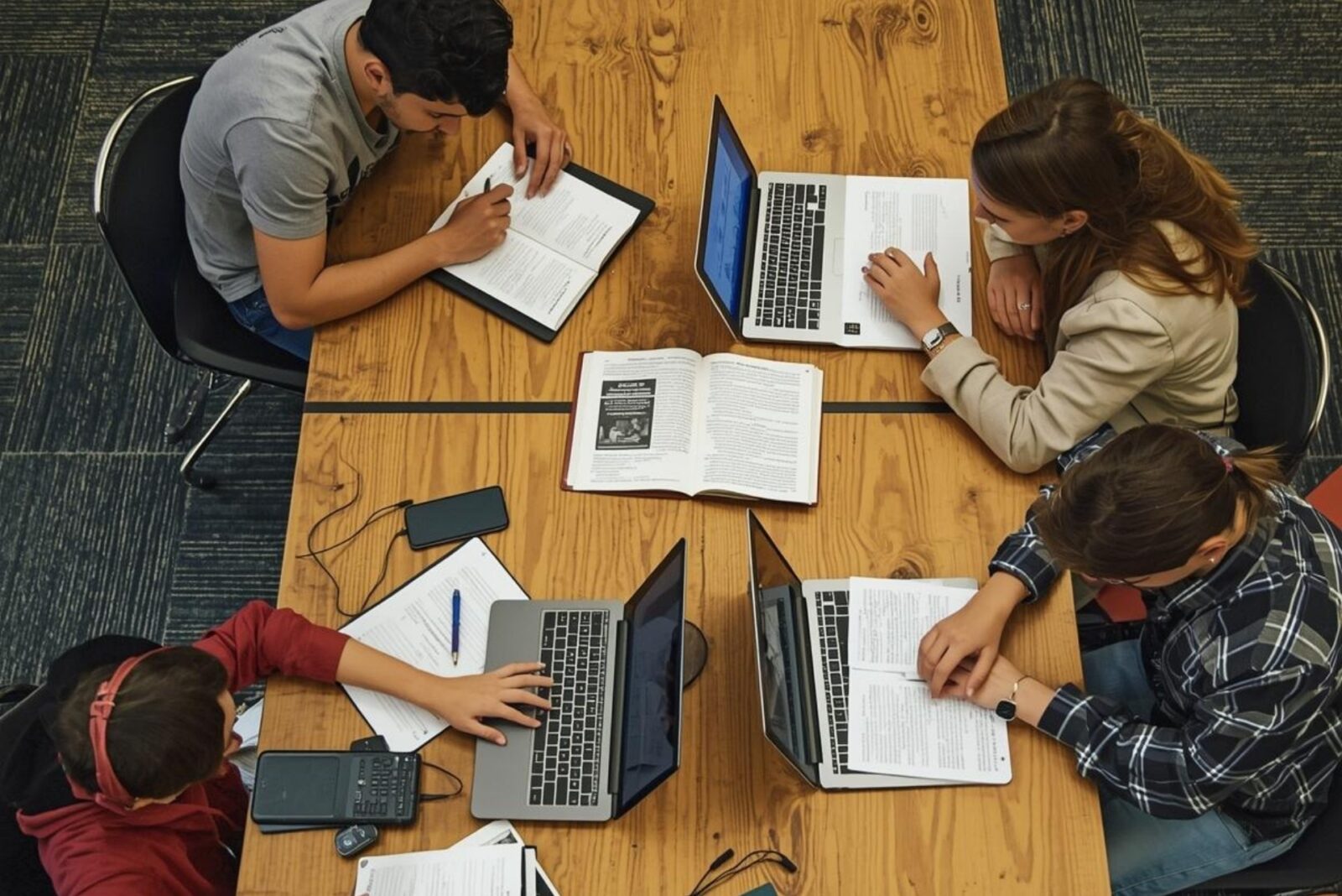 Modern student group studying with laptops and books at a wooden table in a university setting.